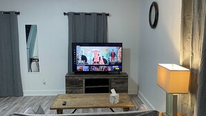 Ein Wohnzimmer mit Flachbildfernseher, einer Couch, einem Couchtisch, einer Lampe und einer Wanduhr.