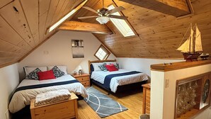 A cozy attic bedroom with two beds, a wooden ceiling, a skylight, and a ship model on a dresser.