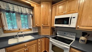 A kitchen with wooden cabinets, a white stove, a microwave, and a sink.