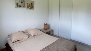 Une chambre à coucher comprenant un lit, une table de chevet, une lampe fixée au mur et deux tableaux encadrés.