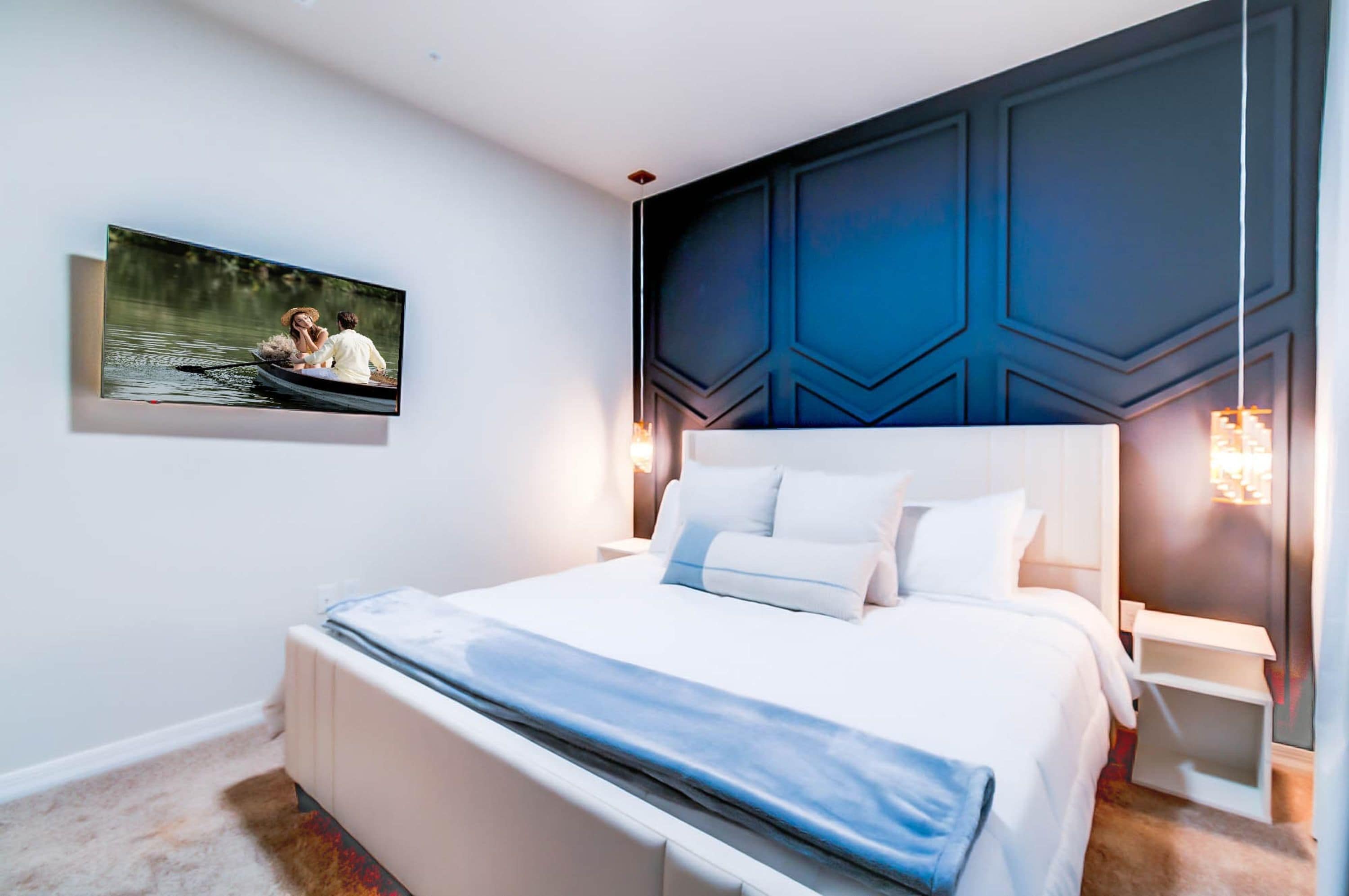 Un dormitorio moderno con una cama grande, un televisor montado en la pared y un revestimiento mural con estampado geométrico.