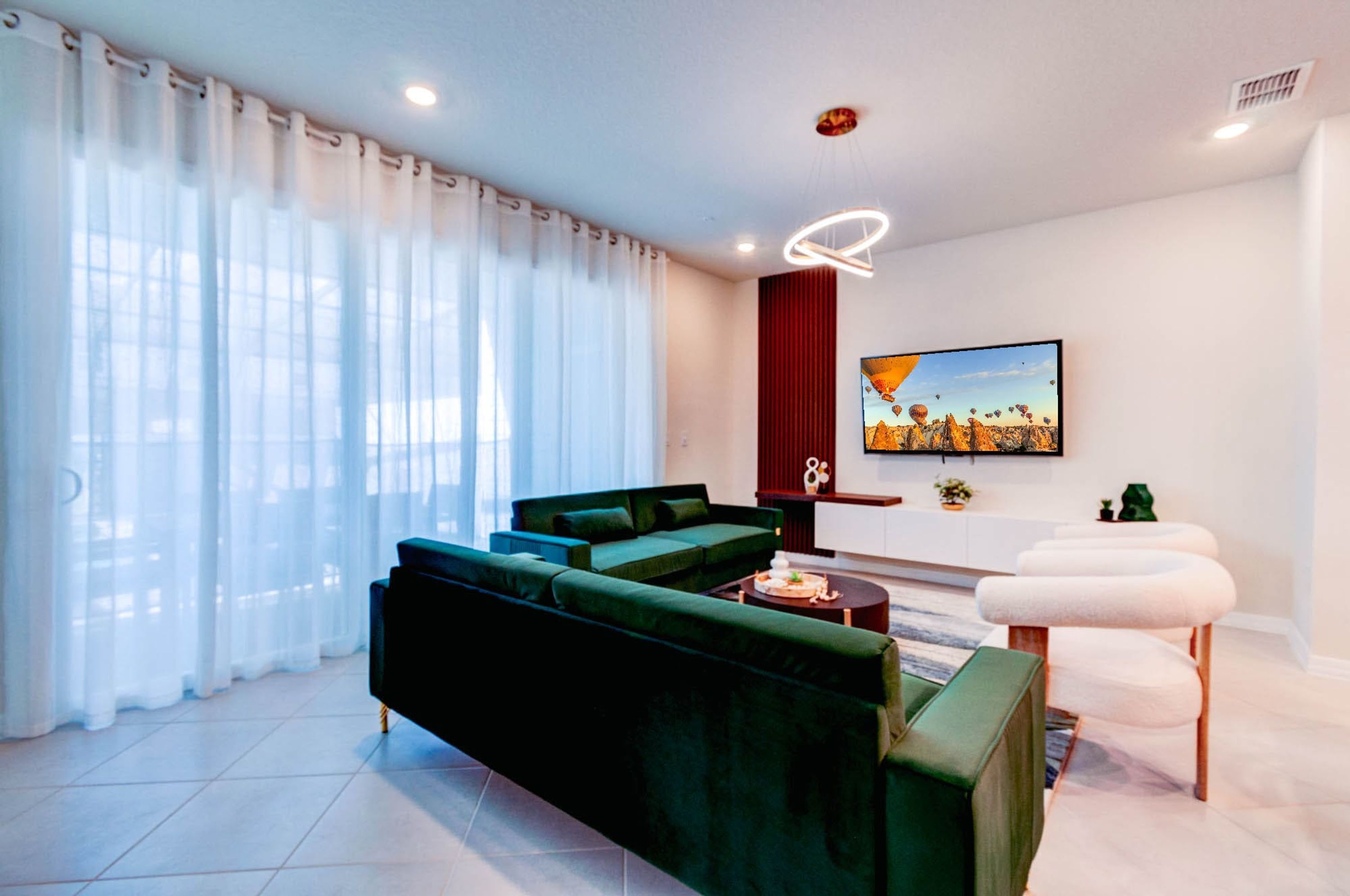 Een moderne woonkamer met een groene bank, een salontafel en een aan de muur bevestigde televisie.