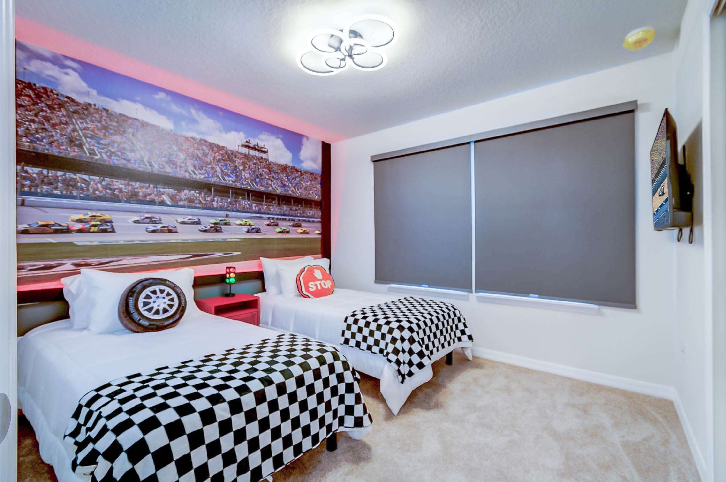 A hotel room with two beds, a large window, a wall mural of a racing event, and a ceiling light fixture.