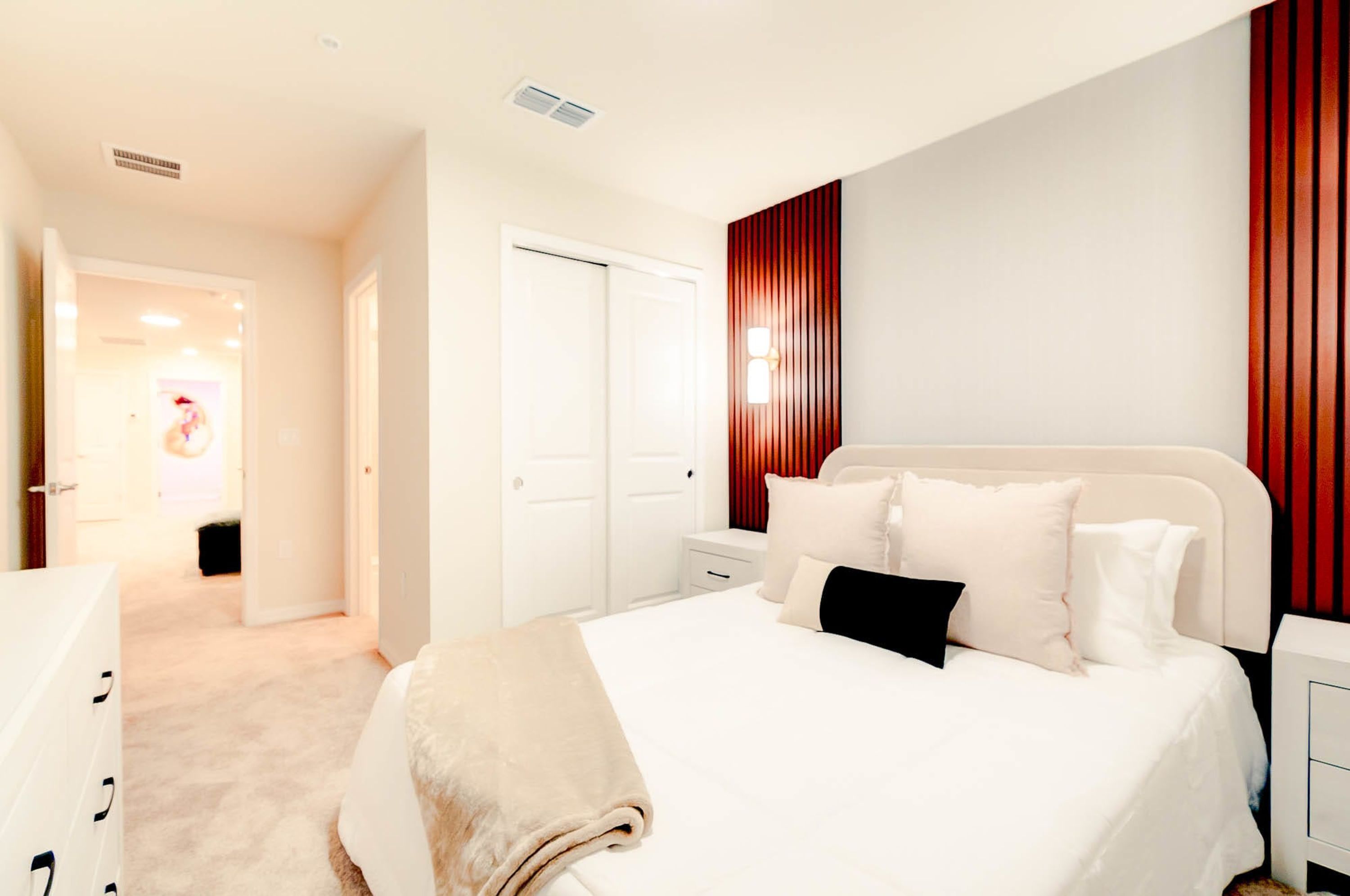 A modern hotel room with a large bed, a bedside table, a wardrobe, and a red accent wall.