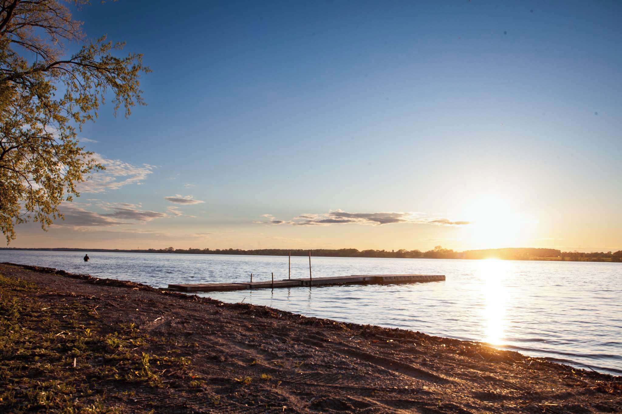 A lakeside view with a dock extending into the water, surrounded by trees and a clear sky.