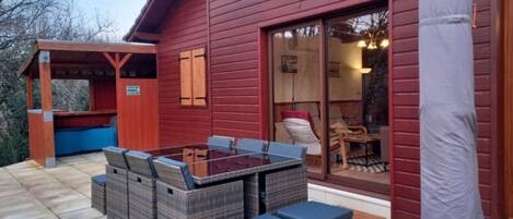 A red wooden building with a covered patio area, a glass door leading to an interior space, and outdoor furniture.