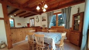 Un comedor de madera con una mesa, sillas, una ventana con cortinas y un aparador con puertas de cristal.