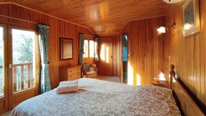 Dormitorio de cabaña de madera con cama, cómoda, silla y ventana con cortinas.