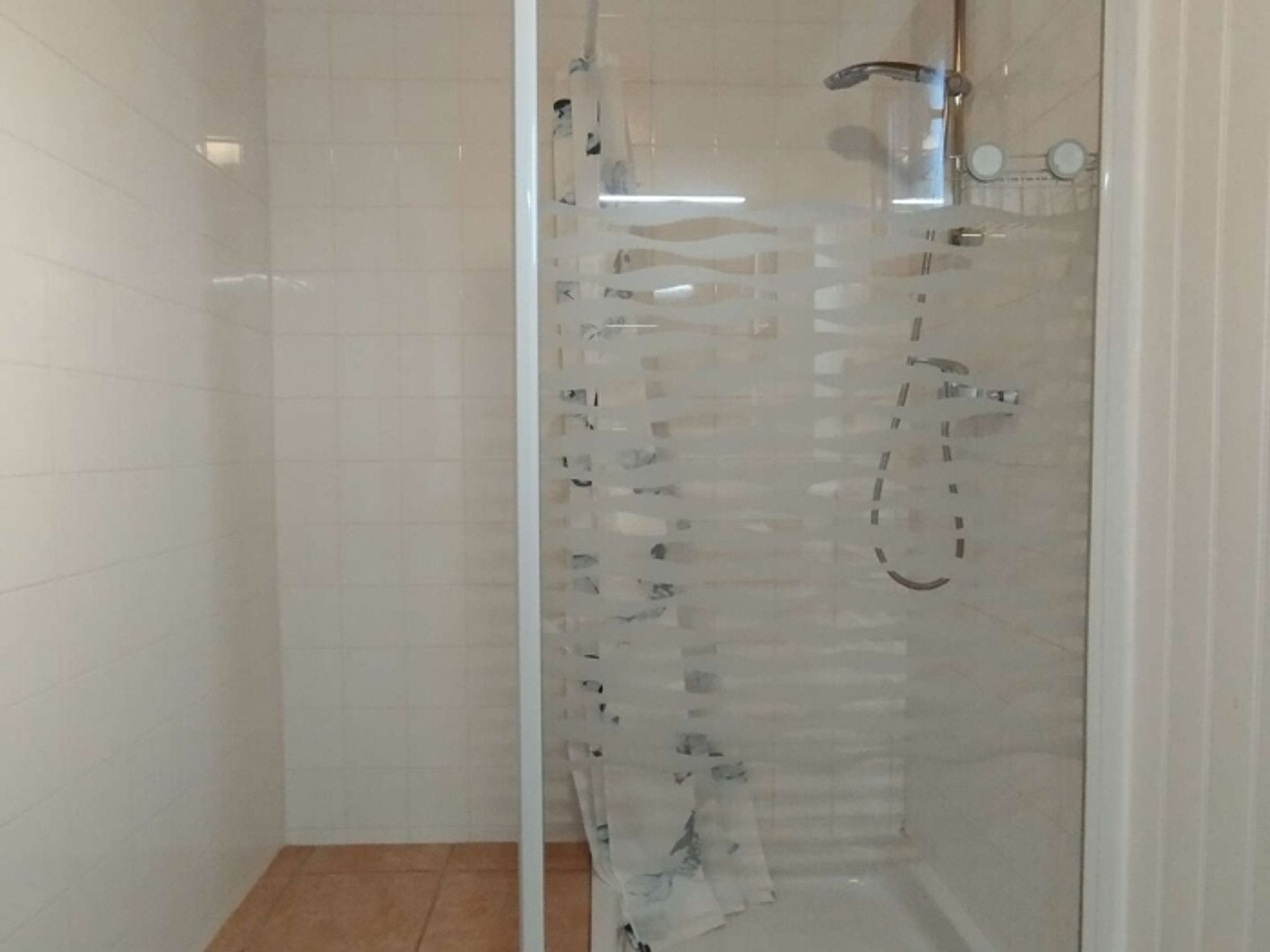 Eine Duschkabine mit Glaswänden, einer Handbrause und einem am Wand montierten Wasserhahn.