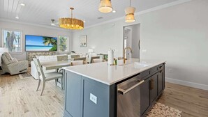 Una cocina moderna con una isla central, luces colgantes y un comedor con vista al océano.