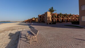 A beachfront hotel with a paved walkway, palm trees, and a bench. - ALAHLAM CHALET YANBU (Yanbu)