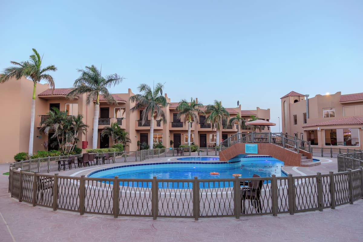 A hotel with a swimming pool, palm trees, and a fenced patio area.