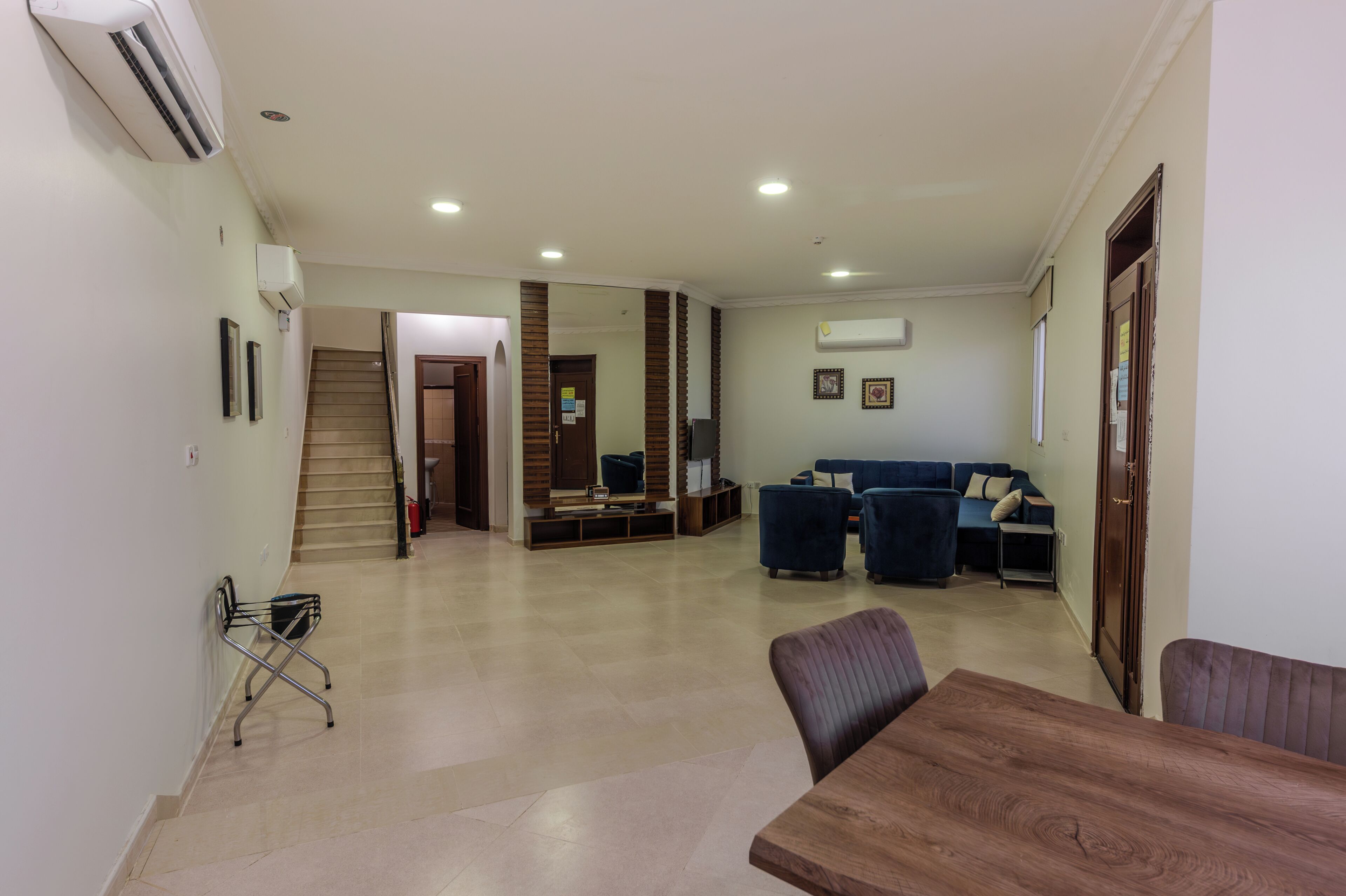 Amplia sala de estar con una mesa de comedor de madera, sofás azules, una escalera y un pasillo que conduce a otra habitación.