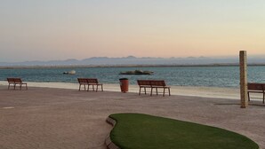 A paved walkway with benches and a grassy area by a body of water, with mountains in the background. - ALAHLAM CHALET YANBU (Yanbu)