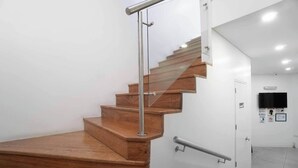 Una scala moderna con gradini in legno e ringhiere in metallo, che conduce a una porta bianca con una targa nera sopra.