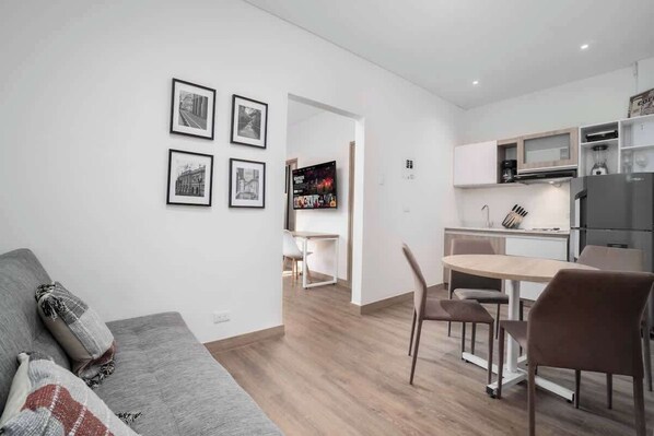 A modern living room with a grey sofa, a dining area with a table and chairs, and a kitchen with a refrigerator and microwave. - M202 - Río Bulevar | Zona Rosa and Historic Center (Cali)