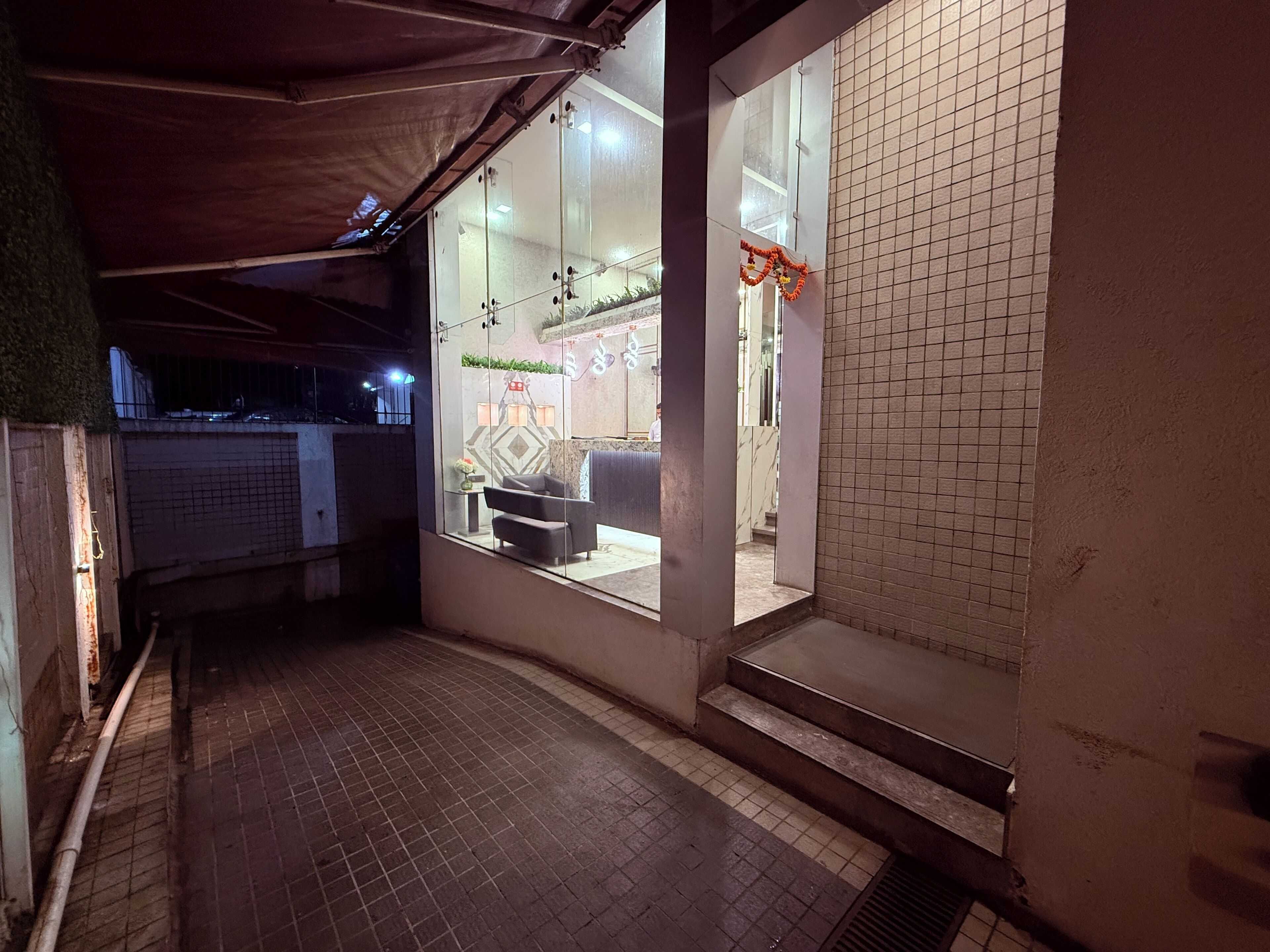 A corridor with tiled flooring, a seating area with a sofa and table, and a glass door leading to a room with a patterned wall and a small plant.