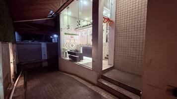 A corridor with tiled flooring, a seating area with a sofa and table, and a glass door leading to a room with a patterned wall and a small plant.
