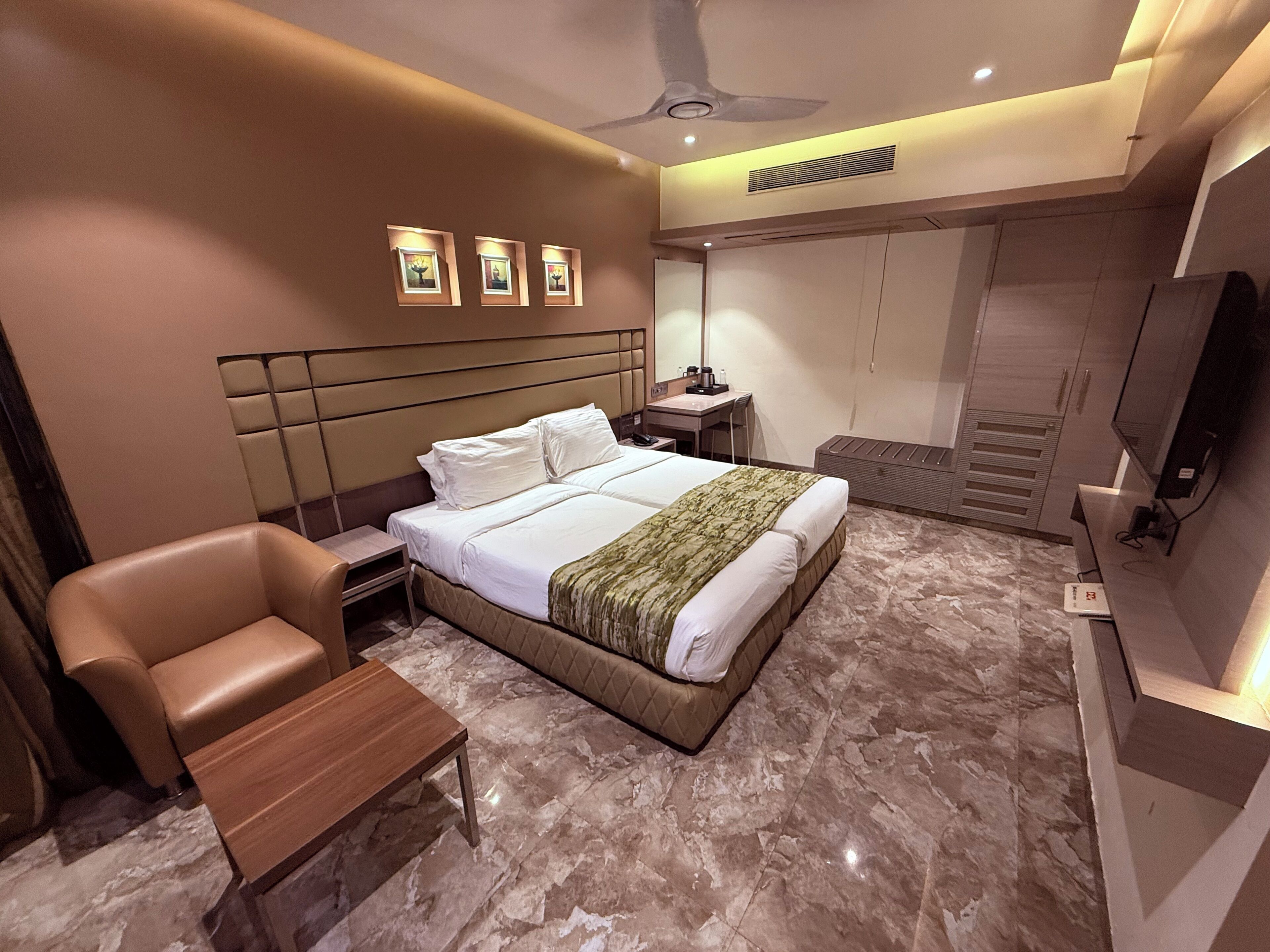 A modern hotel room with a bed, a desk, a chair, a TV, and a ceiling fan.