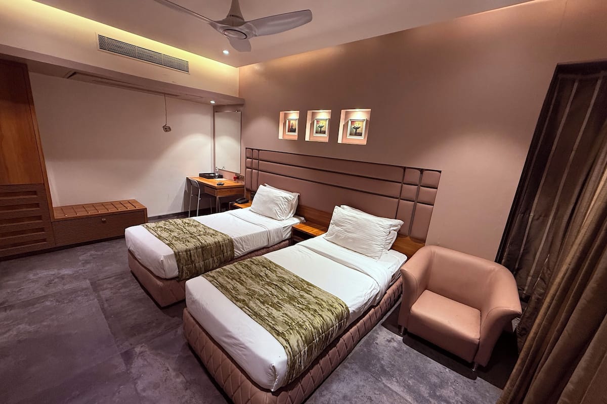 A hotel room with two beds, a desk, a chair, and a ceiling fan.