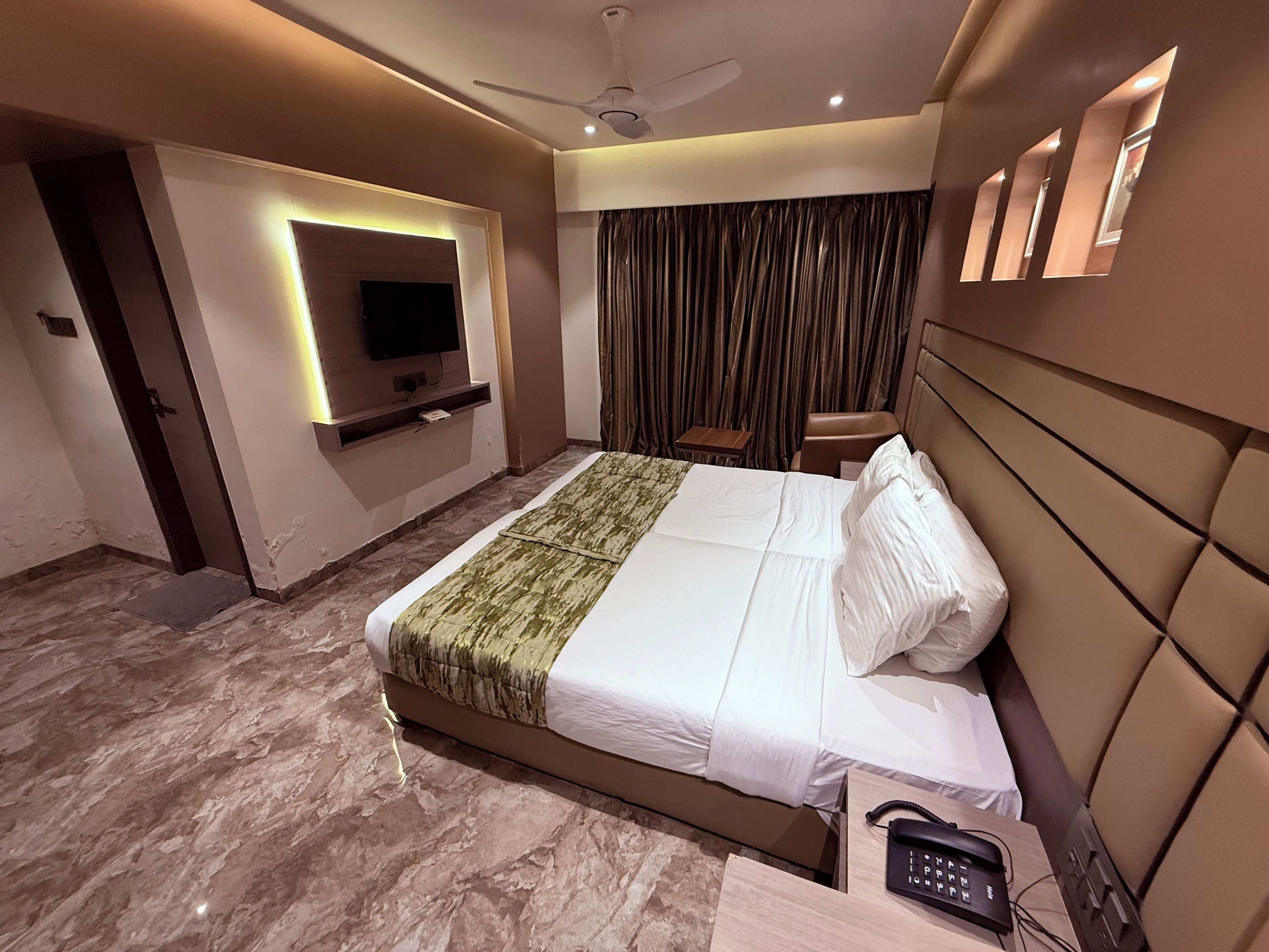 Habitación de hotel moderna con una cama grande, un televisor de pantalla plana, un ventilador de techo y un teléfono junto a la cama.