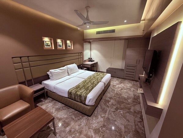 A modern hotel room with a large bed, a desk, a chair, a vanity, and a television. - Hotel Varishtta (Navi Mumbai)