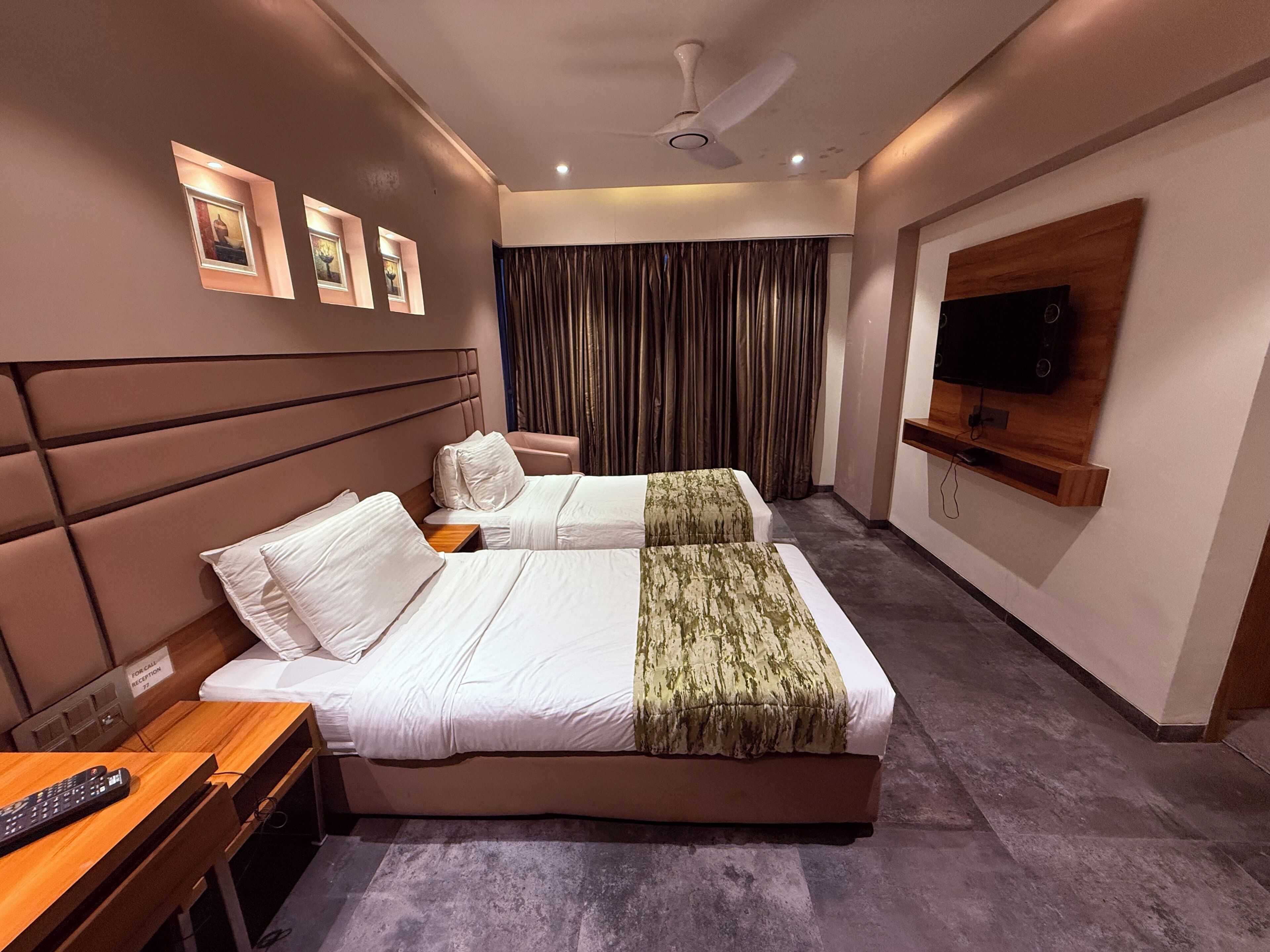 Ein Hotelzimmer mit zwei Betten, einem an der Wand befestigten Fernseher, einem Deckenventilator und einem Empfangsschild.
