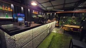 A bar area with a counter, a Pepsi refrigerator, and a seating area with a green wall and plants. - Hotel Varishtta (Navi Mumbai)