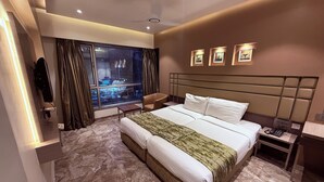 A modern hotel room with a large bed, a desk, a chair, a TV, and a window with curtains. - Hotel Varishtta (Navi Mumbai)