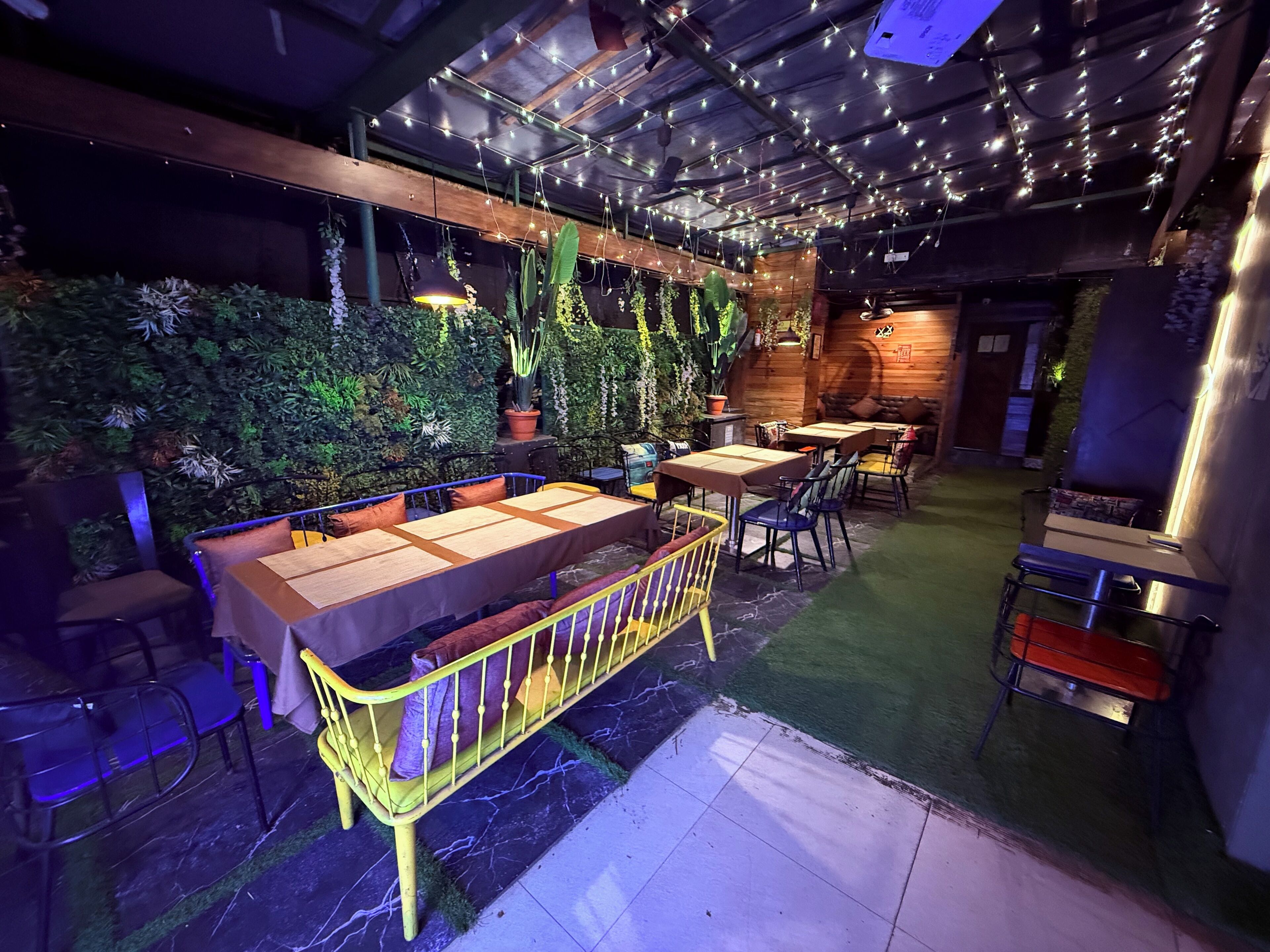Un espacio interior con mesas y sillas, un sofá y una pared decorativa con plantas.