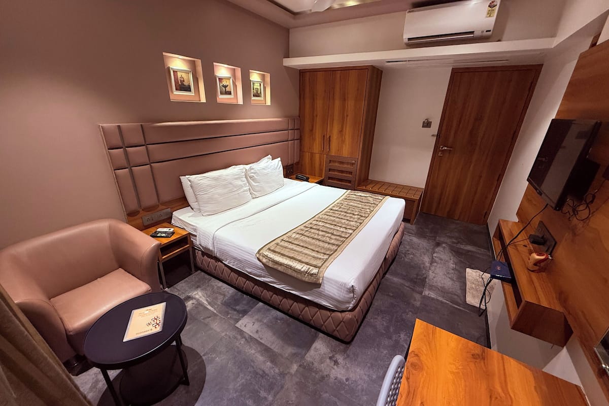 A hotel room with a bed, a chair, a small table, a TV, and a wardrobe.