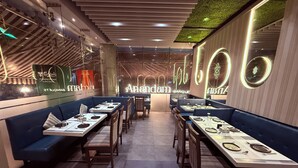 A modern restaurant interior with blue booths and long tables, featuring a neon sign and a green ceiling. - Hotel Varishtta (Navi Mumbai)