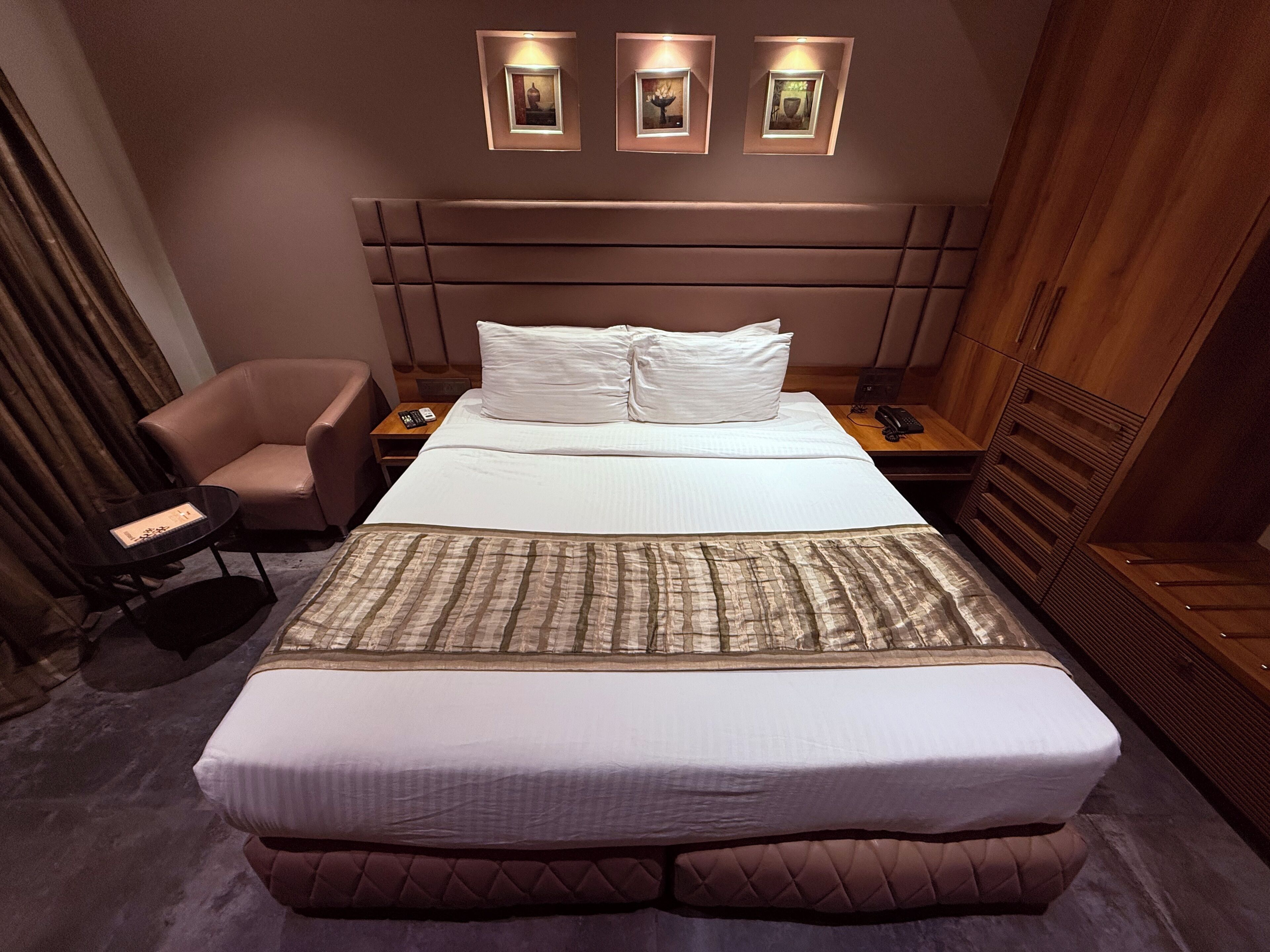 A hotel room with a large bed, a chair, a bedside table, and a wardrobe.