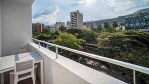 A balcony with a table and chairs, overlooking a cityscape with buildings and greenery.