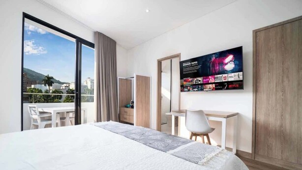 A modern hotel room with a large bed, a desk, and a TV displaying a movie poster.