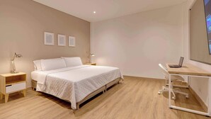 A bedroom with a bed, bedside tables, a desk with a laptop, and a TV on the wall.
