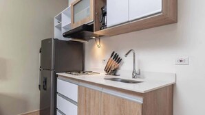 A compact kitchen with a built-in refrigerator, a sink, and wooden cabinetry. - M401 - Studio | River Boulevard | Balcony | Fun (Cali)