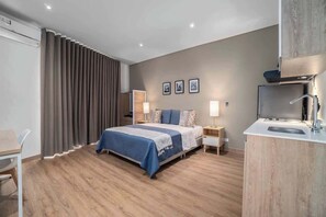 A modern hotel room with a bed, bedside tables, a desk, and a kitchenette. - M401 - Studio | River Boulevard | Balcony | Fun (Cali)