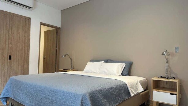 Een slaapkamer met een bed, nachtkastjes, een airconditioner en een houten garderobe.