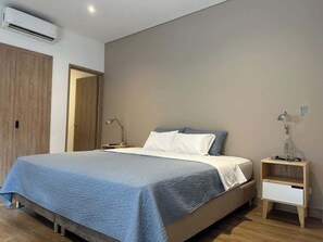 Une chambre à coucher comprenant un lit, des tables de chevet, un appareil de climatisation et une armoire en bois.