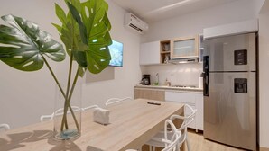 Een moderne keuken met witte kasten, een roestvrijstalen koelkast en een eethoek met een houten tafel en witte stoelen.