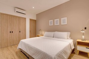 A bedroom with a bed, wooden wardrobe, bedside tables, and an air conditioning unit.