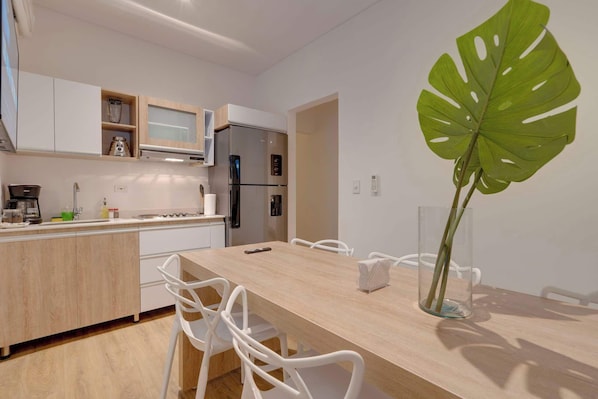 A modern kitchen with white cabinets, a stainless steel refrigerator, and a wooden dining table with white chairs.