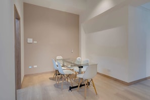 A modern room with a glass table and white chairs, a wooden floor, and a plain wall with a light switch. - M502 | Amazing 2-Bed Apartment | River Boulevard (Cali)