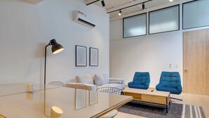 Una sala de reuniones moderna con una mesa de vidrio, sillas, un sofá y dos sillones azules.