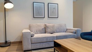 Una sala de estar moderna con un sofá, una mesa de centro, una lámpara de pie y dos obras de arte enmarcadas en la pared.