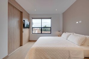 Une chambre à coucher avec un lit, un téléviseur fixé au mur, une fenêtre et une table de chevet.