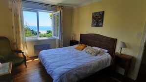Un dormitorio con una cama grande, una silla, un ventanal con vistas al mar y un cuadro en la pared.