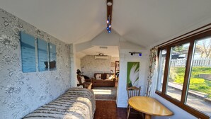 A cozy living room with a sofa, a dining table with chairs, and a view of a garden through large windows. - OYO Lavender House Hotel (Newton Abbot)