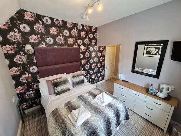 A bedroom with a bed, a vanity with a mirror, and a wall with floral wallpaper. - OYO Lavender House Hotel (Newton Abbot)